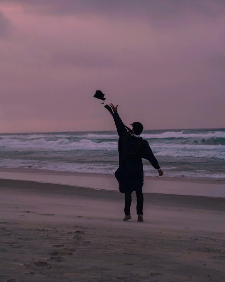 A man standing on the beach at sunset, tossing something off into the horizon